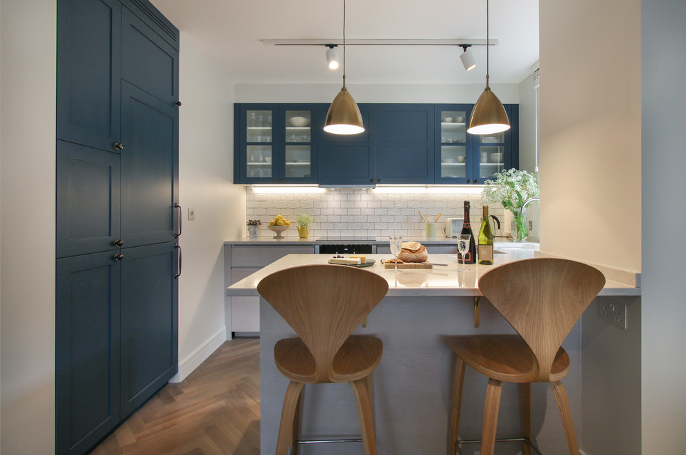 This is an example of a medium sized contemporary u-shaped open plan kitchen in London with white splashback, metro tiled splashback, shaker cabinets, blue cabinets, quartz worktops, integrated appliances, light hardwood flooring, an island and turquoise worktops.