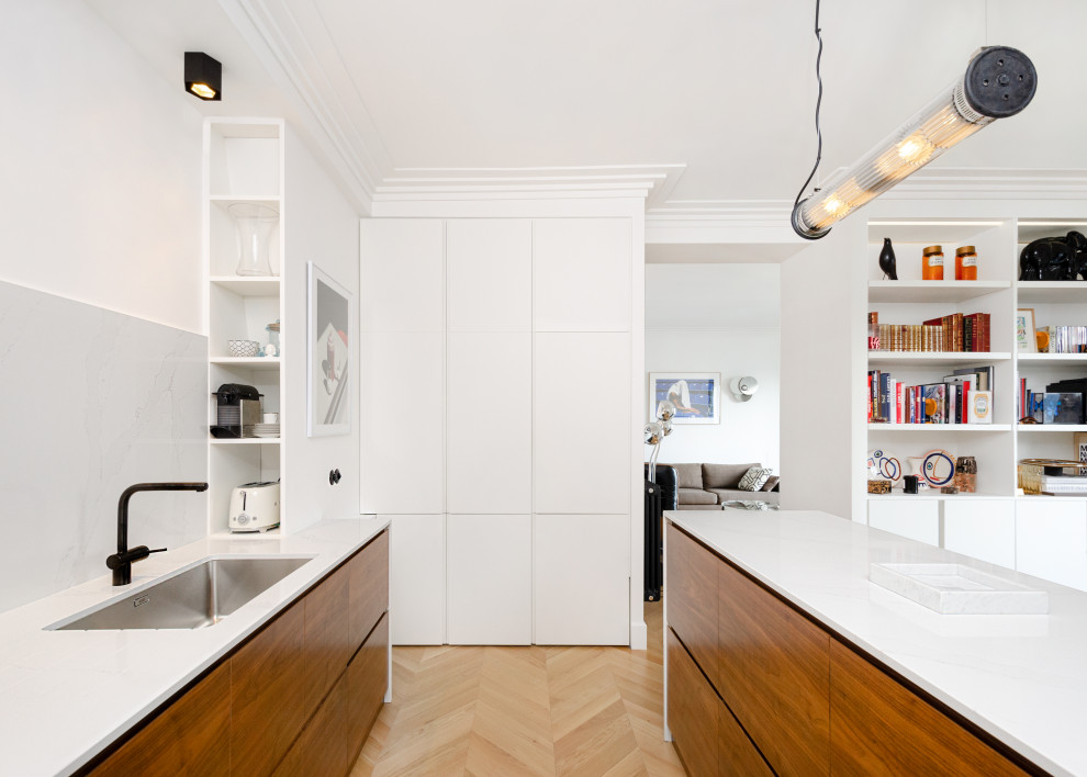Example of a small danish single-wall light wood floor and beige floor open concept kitchen design in Paris with an undermount sink, flat-panel cabinets, dark wood cabinets, marble countertops, white backsplash, marble backsplash, black appliances, an island and white countertops