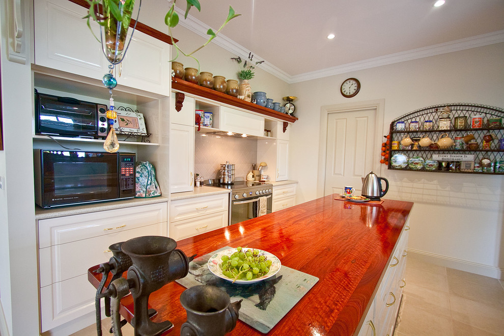 Immagine di una cucina parallela classica con ante con bugna sagomata, ante beige, top in legno, paraspruzzi beige e elettrodomestici in acciaio inossidabile