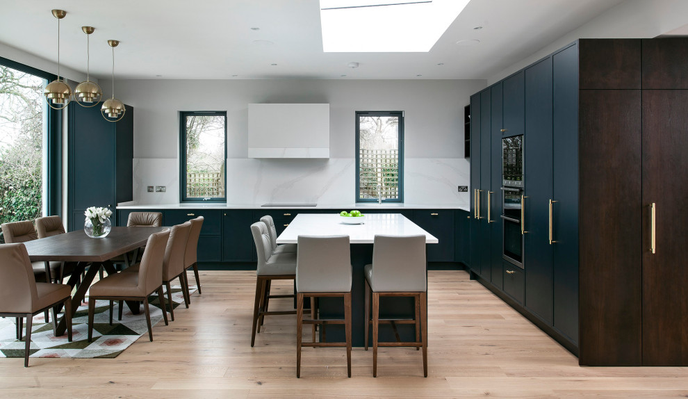 Example of a large trendy l-shaped light wood floor and beige floor eat-in kitchen design in Dublin with an undermount sink, flat-panel cabinets, dark wood cabinets, quartzite countertops, white backsplash, black appliances, an island and white countertops