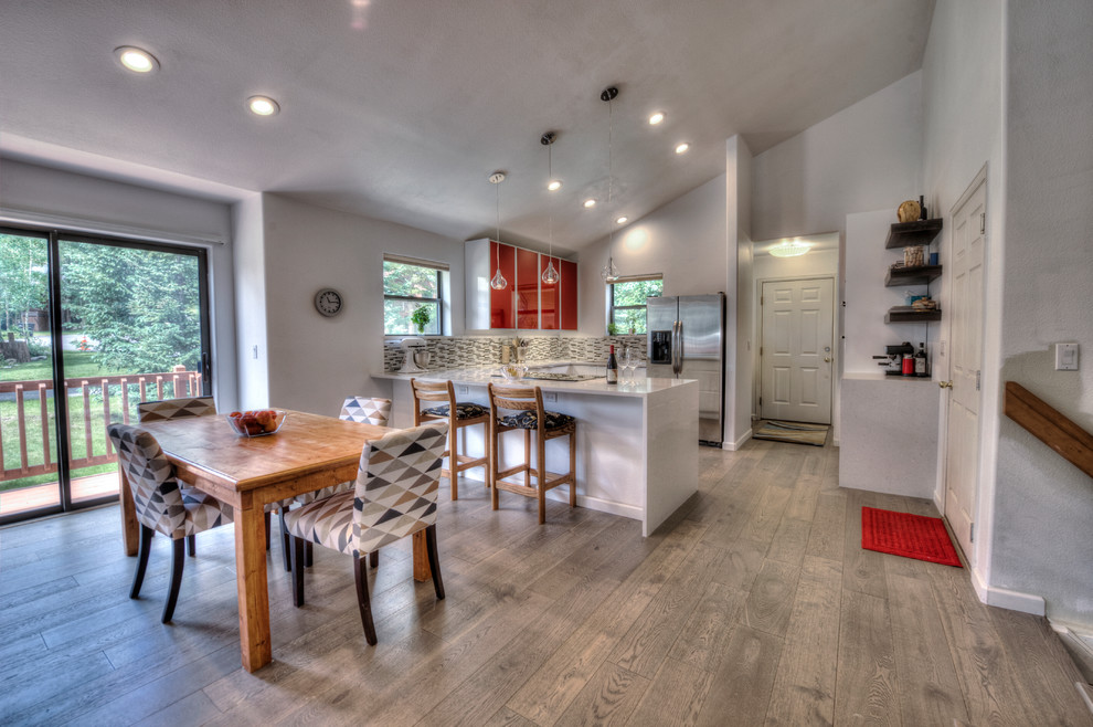 This is an example of a medium sized contemporary u-shaped kitchen/diner in Denver with a submerged sink, flat-panel cabinets, red cabinets, engineered stone countertops, multi-coloured splashback, matchstick tiled splashback, stainless steel appliances, medium hardwood flooring and a breakfast bar.