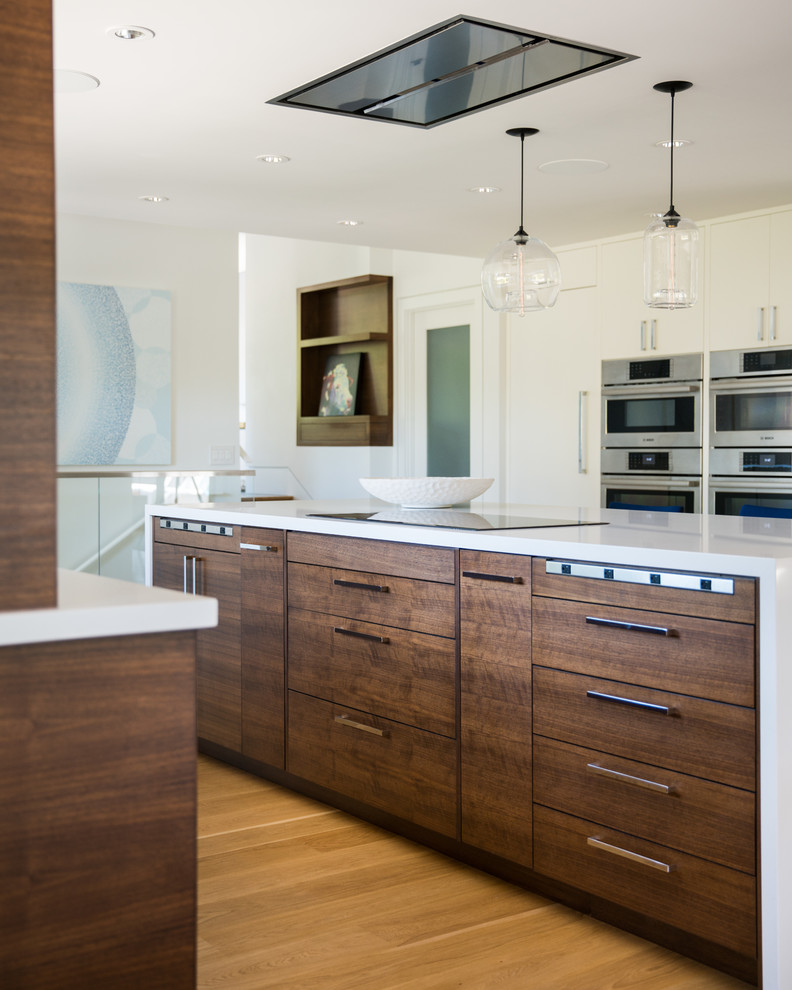 This is an example of a medium sized contemporary galley kitchen/diner in San Francisco with flat-panel cabinets, dark wood cabinets, stainless steel appliances, medium hardwood flooring, an island, brown floors, white worktops, composite countertops and a submerged sink.