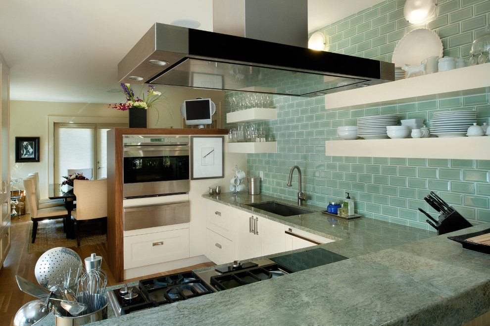Amerikansk inredning av ett mellanstort kök, med en enkel diskho, luckor med infälld panel, vita skåp, grönt stänkskydd, stänkskydd i tunnelbanekakel, rostfria vitvaror, ljust trägolv, marmorbänkskiva och en halv köksö