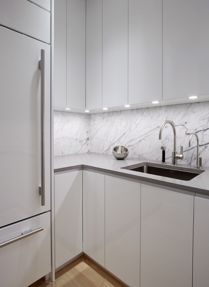 Inspiration for a small modern u-shaped light wood floor enclosed kitchen remodel in New York with an undermount sink, flat-panel cabinets, white cabinets, quartz countertops, white backsplash, stone slab backsplash, stainless steel appliances and no island