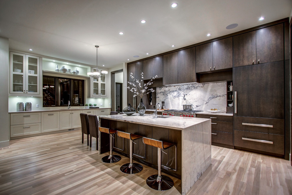 Design ideas for a traditional galley kitchen in Calgary with flat-panel cabinets, dark wood cabinets, grey splashback, stainless steel appliances, light hardwood flooring and an island.