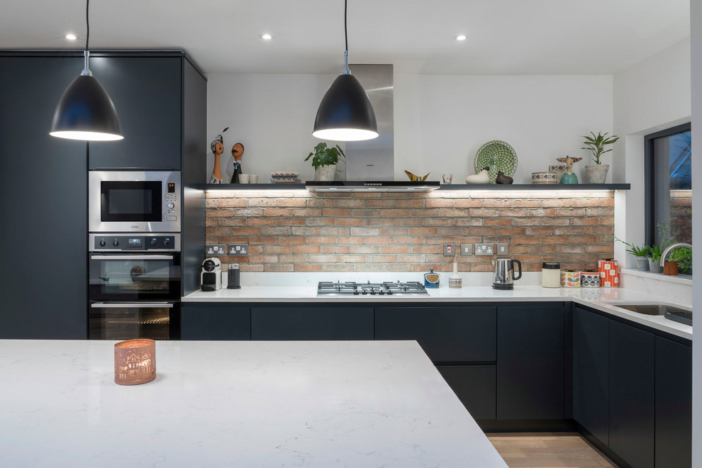 Moderne Küche in L-Form mit flächenbündigen Schrankfronten, Rückwand aus Backstein, weißer Arbeitsplatte, Unterbauwaschbecken, Edelstahlfronten und Kücheninsel in Dublin