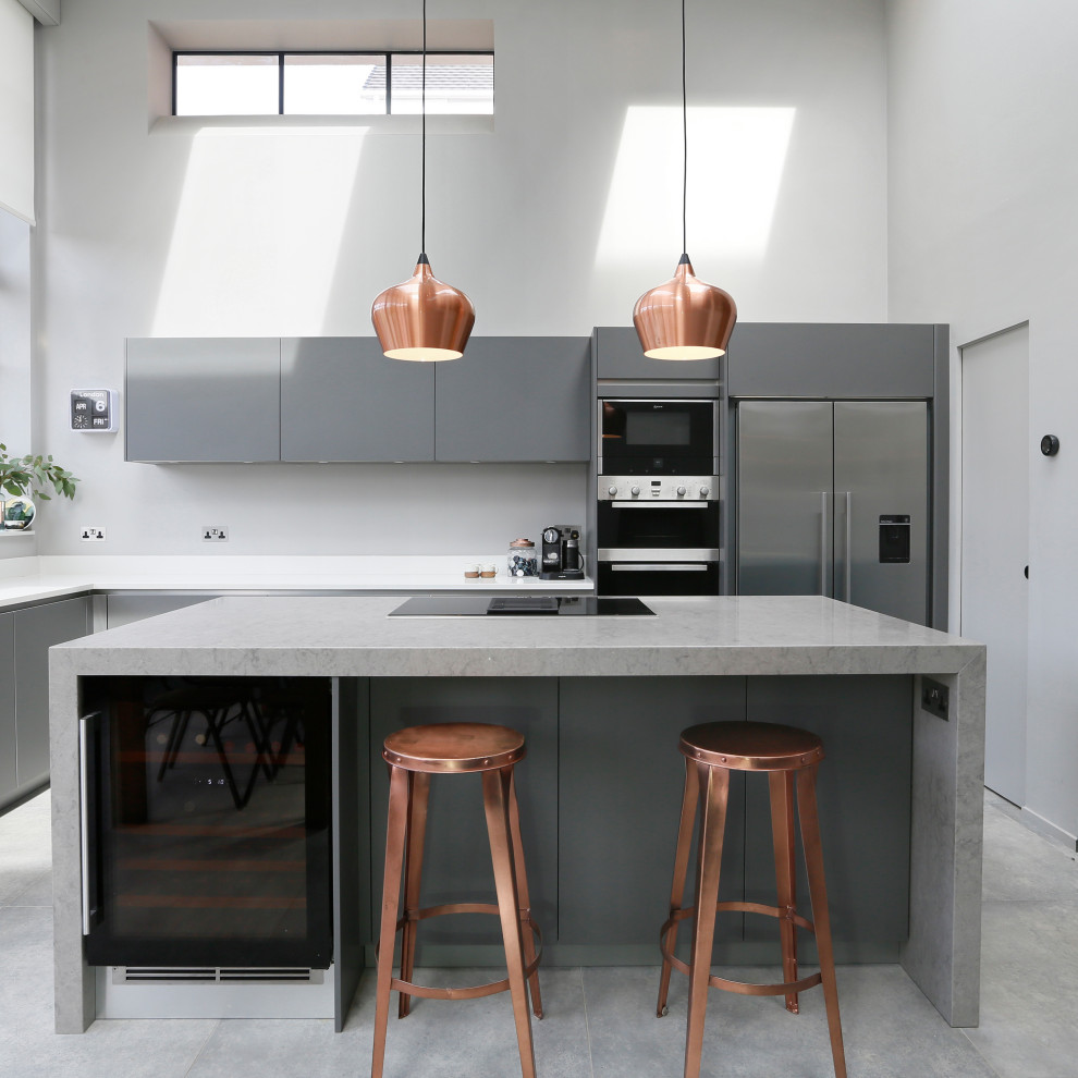 Moderne Küche in L-Form mit flächenbündigen Schrankfronten, grauen Schränken, Küchenrückwand in Grau, Küchengeräten aus Edelstahl, Kücheninsel, grauem Boden und grauer Arbeitsplatte in London
