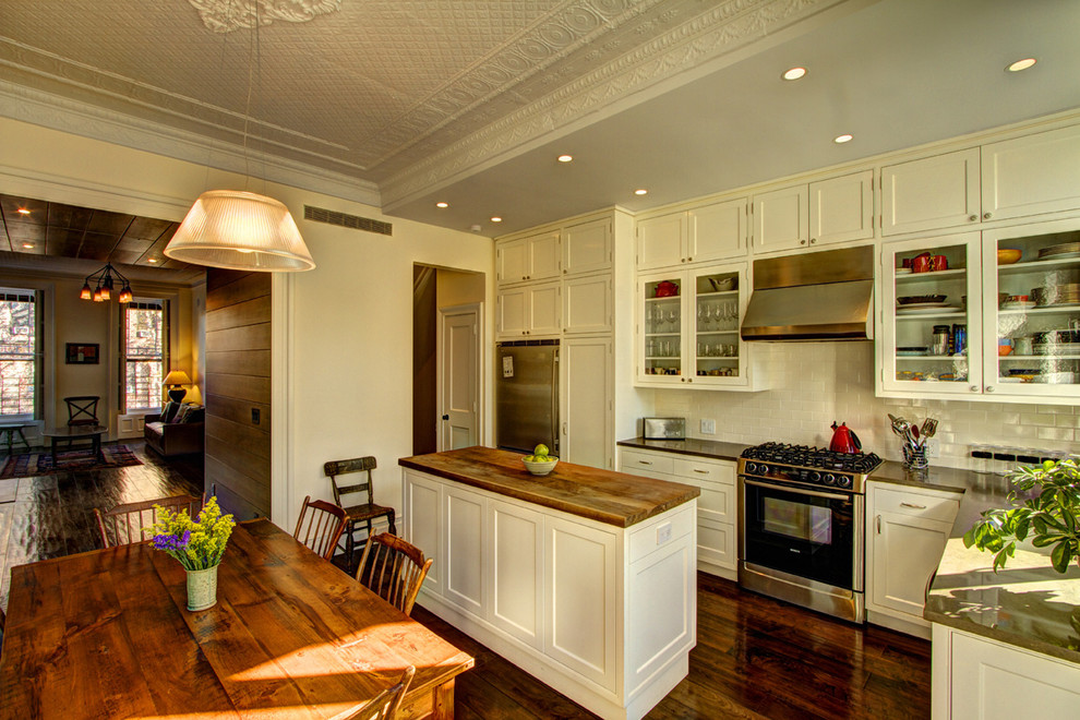 Example of an ornate l-shaped eat-in kitchen design in New York with stainless steel appliances, wood countertops, an undermount sink, shaker cabinets, white cabinets, white backsplash and subway tile backsplash