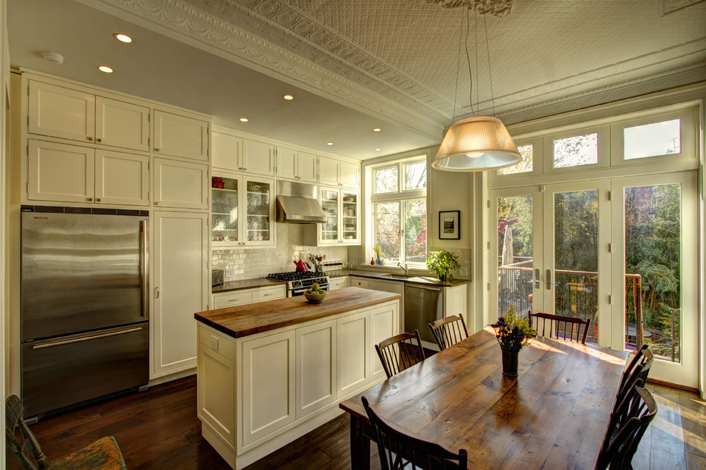 Eat-in kitchen - traditional l-shaped eat-in kitchen idea in New York with stainless steel appliances, wood countertops, an undermount sink, shaker cabinets, white cabinets, white backsplash and subway tile backsplash