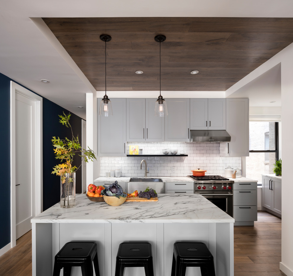 Inspiration for a contemporary kitchen in New York with a belfast sink, shaker cabinets, white cabinets, marble worktops, metro tiled splashback, stainless steel appliances, medium hardwood flooring and a wood ceiling.