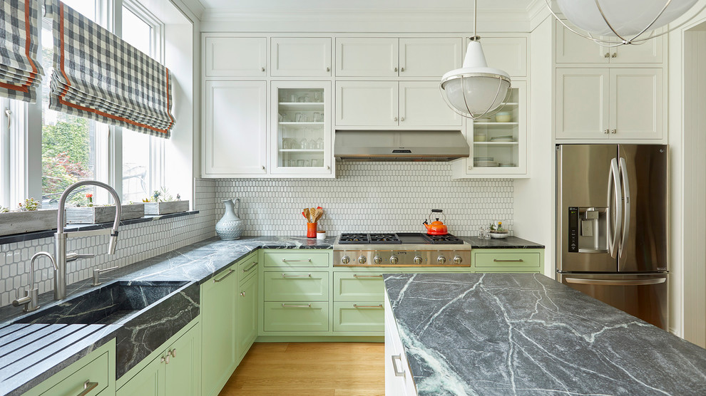 This is an example of a medium sized traditional l-shaped kitchen/diner in New York with an integrated sink, shaker cabinets, green cabinets, soapstone worktops, white splashback, ceramic splashback, stainless steel appliances, light hardwood flooring, an island and brown floors.