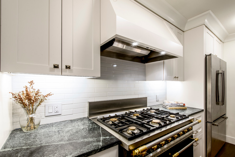 Example of a small classic galley medium tone wood floor kitchen pantry design in New York with an undermount sink, shaker cabinets, medium tone wood cabinets, soapstone countertops, white backsplash, subway tile backsplash, stainless steel appliances and a peninsula