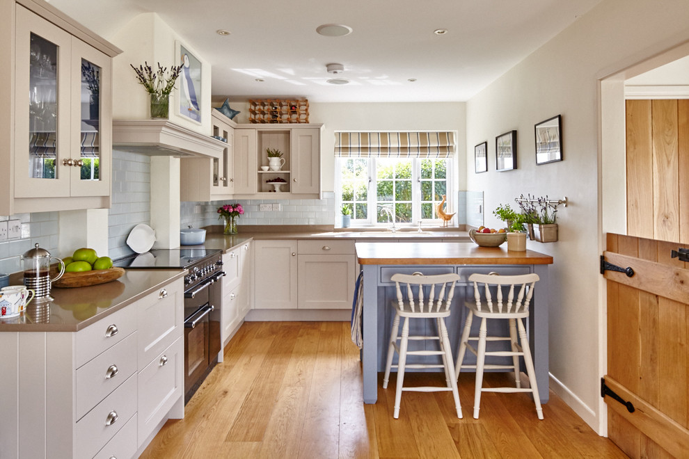 Design ideas for a farmhouse l-shaped kitchen in Berkshire with shaker cabinets, white cabinets, blue splashback, metro tiled splashback, black appliances, medium hardwood flooring and an island.