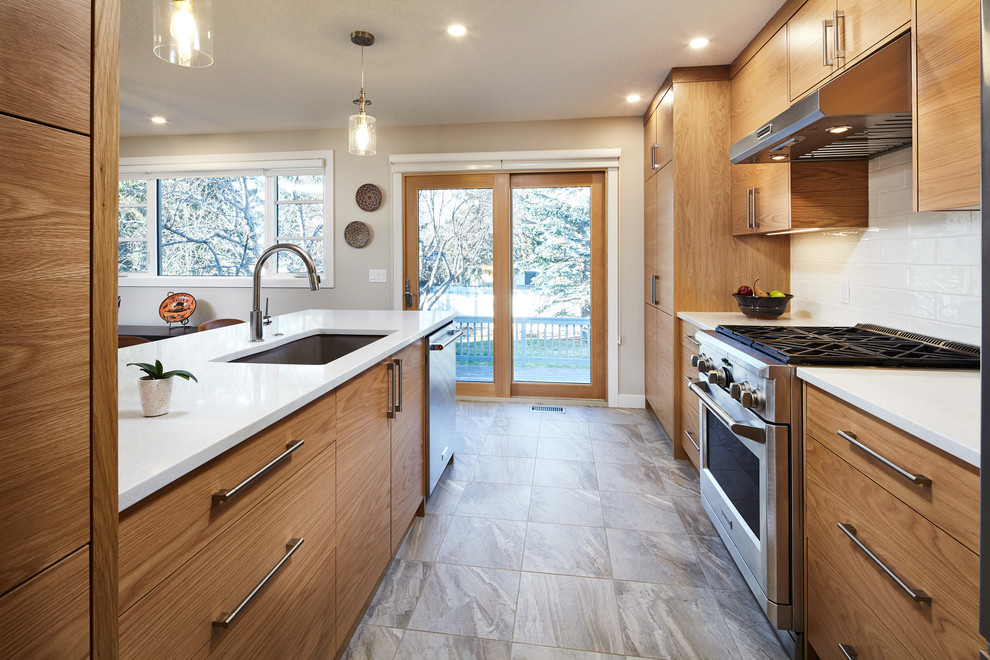 Foto på ett mellanstort vintage vit linjärt kök och matrum, med en undermonterad diskho, släta luckor, skåp i ljust trä, bänkskiva i kvarts, vitt stänkskydd, stänkskydd i tunnelbanekakel, rostfria vitvaror, mellanmörkt trägolv, en halv köksö och brunt golv