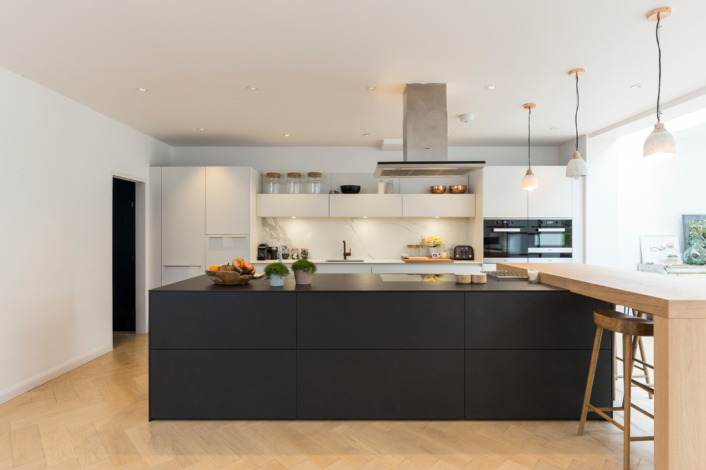Moderne Küche mit flächenbündigen Schrankfronten, Küchenrückwand in Weiß, schwarzen Elektrogeräten, hellem Holzboden und Kücheninsel in London