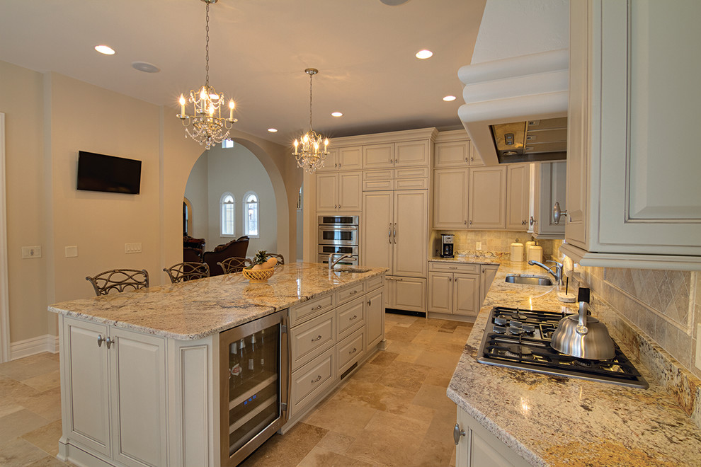 Example of a large tuscan l-shaped limestone floor enclosed kitchen design in Detroit with an undermount sink, raised-panel cabinets, beige cabinets, granite countertops, beige backsplash, stone tile backsplash, stainless steel appliances and an island