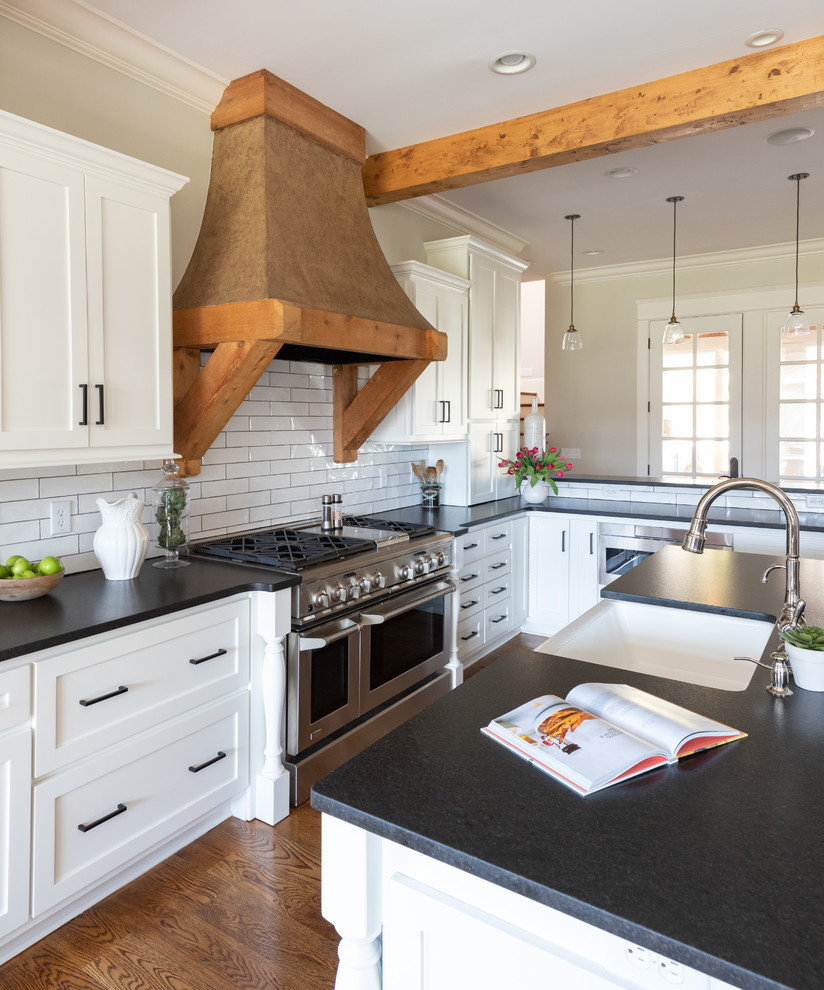 Example of a mid-sized transitional galley medium tone wood floor and brown floor eat-in kitchen design in Nashville with a farmhouse sink, shaker cabinets, white cabinets, quartz countertops, white backsplash, ceramic backsplash, stainless steel appliances, an island and black countertops