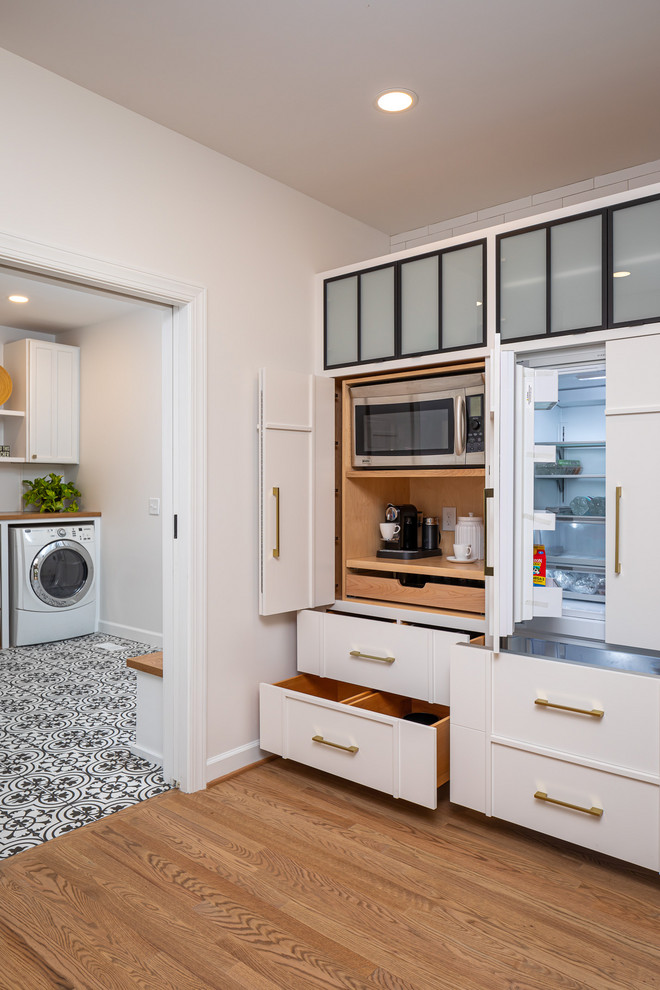 Inspiration for a mid-sized country single-wall light wood floor open concept kitchen remodel in Raleigh with a farmhouse sink, flat-panel cabinets, white cabinets, quartzite countertops, white backsplash, subway tile backsplash, paneled appliances, an island and white countertops