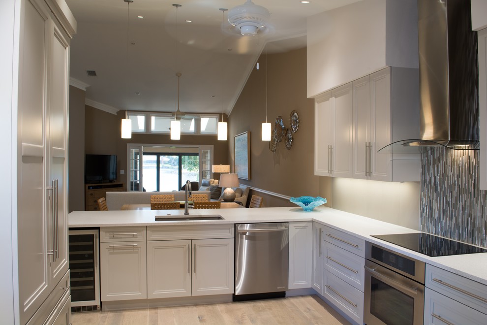 This is an example of a medium sized beach style u-shaped enclosed kitchen in Miami with a submerged sink, recessed-panel cabinets, beige cabinets, composite countertops, multi-coloured splashback, matchstick tiled splashback, integrated appliances, light hardwood flooring, a breakfast bar, beige floors and white worktops.