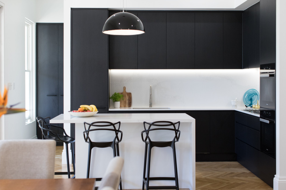 Moderne Küche in L-Form mit Unterbauwaschbecken, flächenbündigen Schrankfronten, schwarzen Schränken, schwarzen Elektrogeräten, braunem Holzboden, Kücheninsel, braunem Boden und weißer Arbeitsplatte in Adelaide