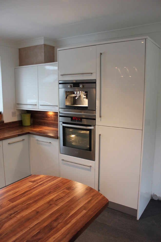 Photo of a medium sized contemporary u-shaped kitchen/diner in Dorset with a built-in sink, flat-panel cabinets, white cabinets, laminate countertops, stainless steel appliances, slate flooring and a breakfast bar.