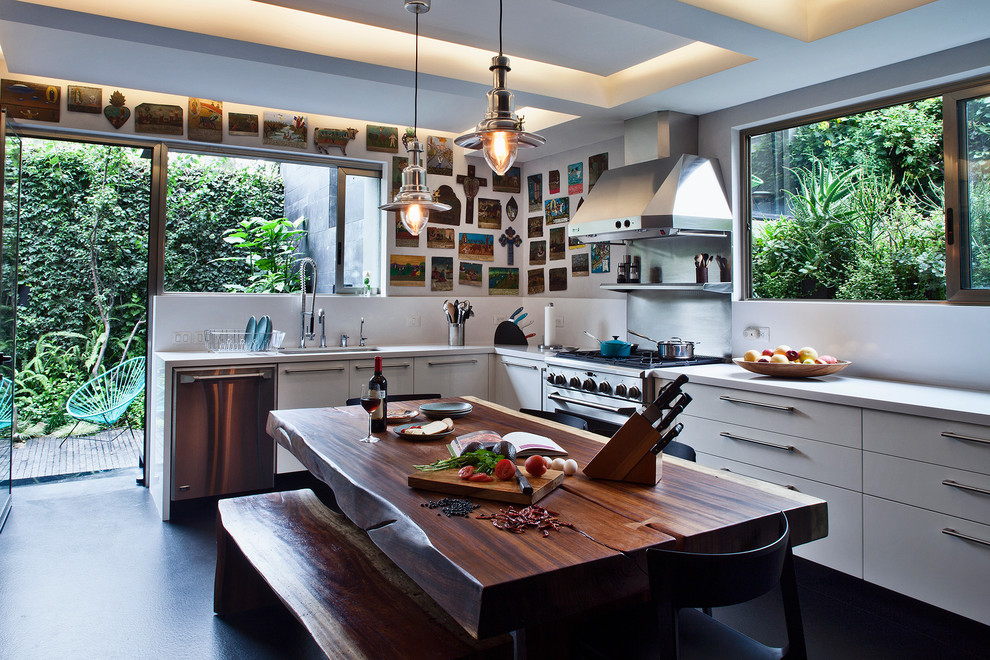 Cette image montre une cuisine américaine design avec un placard à porte plane, des portes de placard blanches, une crédence blanche et un électroménager en acier inoxydable.