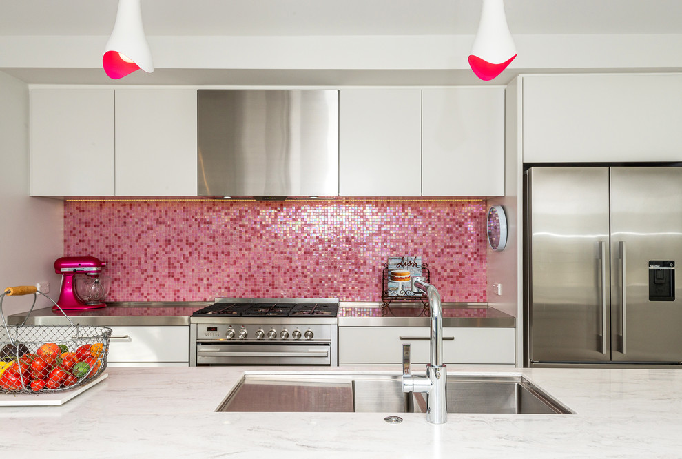 Photo of a small contemporary galley kitchen in Auckland with a submerged sink, flat-panel cabinets, white cabinets, composite countertops, pink splashback, mosaic tiled splashback, stainless steel appliances, ceramic flooring and an island.