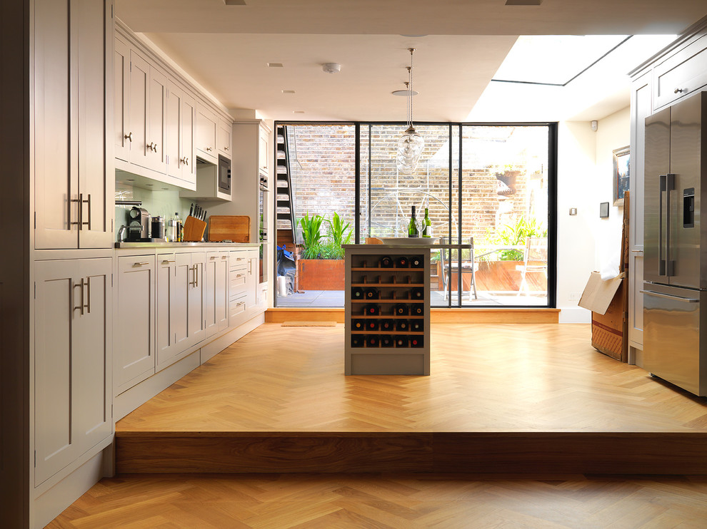 Idées déco pour une cuisine parallèle classique avec un placard à porte shaker, des portes de placard grises, un sol en bois brun et îlot.