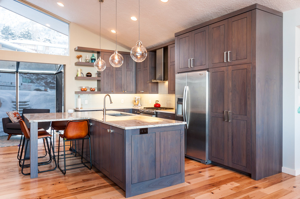 Bild på ett funkis kök, med skåp i shakerstil, grå skåp, rostfria vitvaror, en köksö, en undermonterad diskho, granitbänkskiva, vitt stänkskydd, ljust trägolv och beiget golv