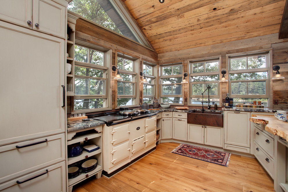 Bild på ett mellanstort rustikt kök, med en rustik diskho, skåp i slitet trä, granitbänkskiva, stänkskydd med metallisk yta, stänkskydd i metallkakel, integrerade vitvaror, ljust trägolv och en halv köksö