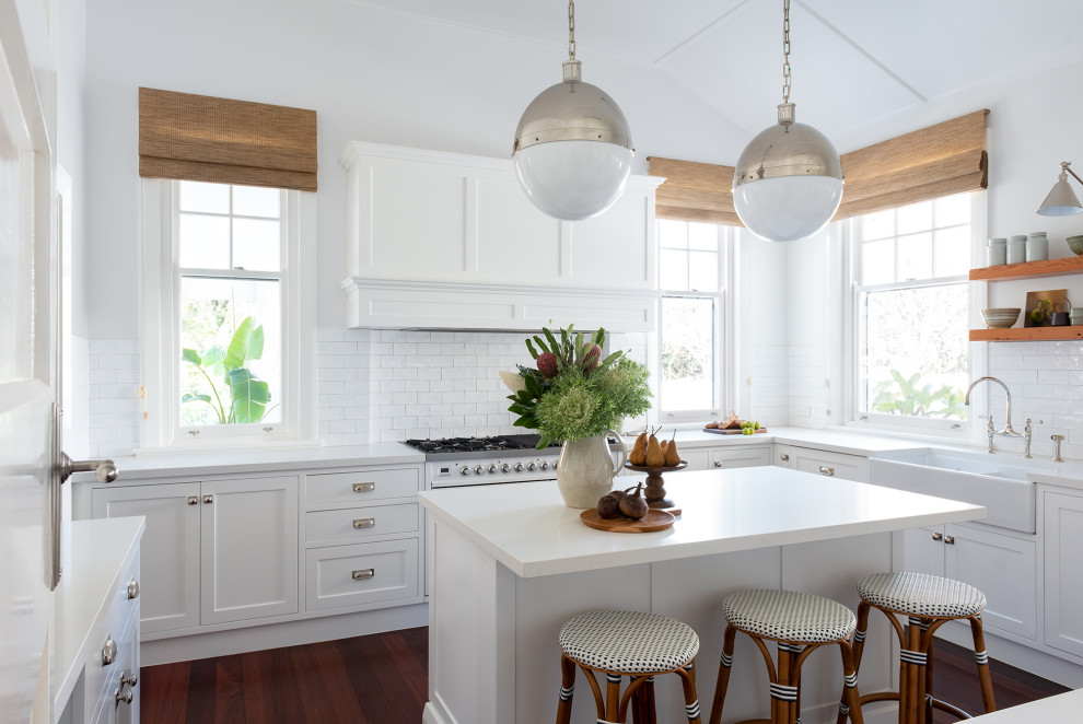 Foto på ett kök, med en rustik diskho, skåp i shakerstil, vita skåp, vitt stänkskydd, vita vitvaror och en köksö