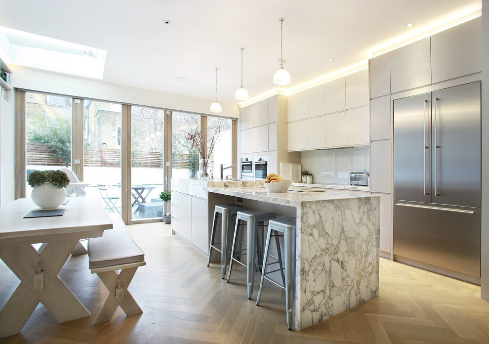 Zweizeilige Moderne Wohnküche mit flächenbündigen Schrankfronten, weißen Schränken, Küchenrückwand in Weiß, Glasrückwand und Küchengeräten aus Edelstahl in London