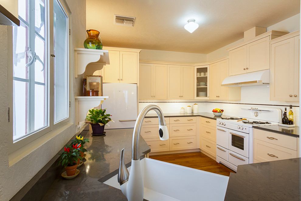 Example of a mid-sized cottage l-shaped medium tone wood floor and brown floor eat-in kitchen design in Phoenix with a farmhouse sink, shaker cabinets, yellow cabinets, quartz countertops, white backsplash, subway tile backsplash, white appliances and no island