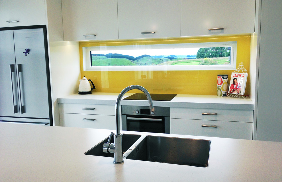 Photo of a medium sized modern single-wall open plan kitchen in Other with a double-bowl sink, flat-panel cabinets, white cabinets, laminate countertops, yellow splashback, glass sheet splashback, white appliances, concrete flooring and an island.