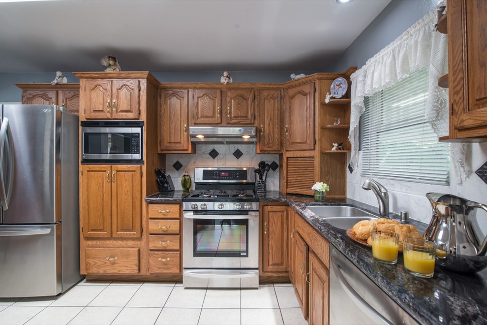 Example of a classic u-shaped eat-in kitchen design in San Diego with a drop-in sink, raised-panel cabinets, medium tone wood cabinets, granite countertops, white backsplash and stainless steel appliances
