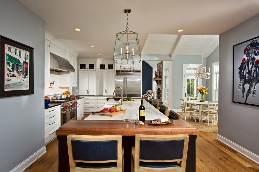 Einzeilige Klassische Küche mit Landhausspüle, Kassettenfronten, weißen Schränken, Marmor-Arbeitsplatte, Küchenrückwand in Weiß, Küchengeräten aus Edelstahl, braunem Holzboden und Kücheninsel in Boston