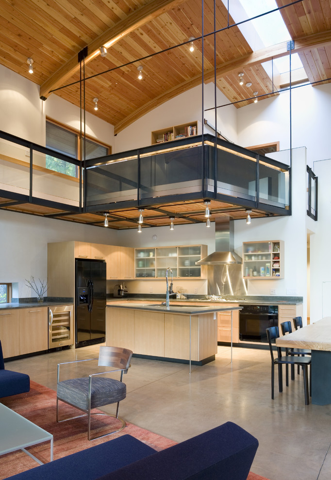 Example of a mid-sized trendy l-shaped concrete floor open concept kitchen design in Seattle with black appliances, glass-front cabinets, light wood cabinets, metallic backsplash, metal backsplash, solid surface countertops and an island