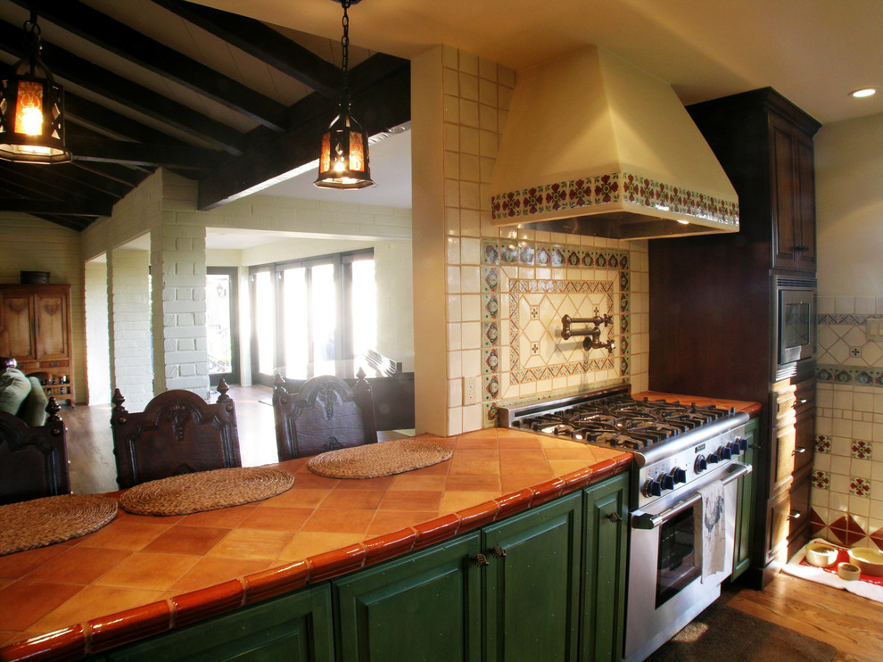 Example of a large tuscan medium tone wood floor kitchen design in Los Angeles with a peninsula, raised-panel cabinets, green cabinets, white backsplash, stainless steel appliances and a drop-in sink