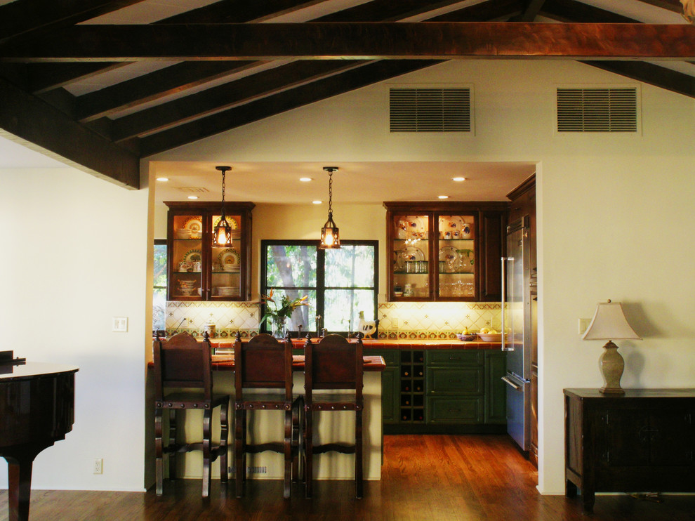 Large tuscan medium tone wood floor kitchen photo in Los Angeles with a peninsula, raised-panel cabinets, green cabinets, tile countertops, yellow backsplash, ceramic backsplash, stainless steel appliances and a drop-in sink