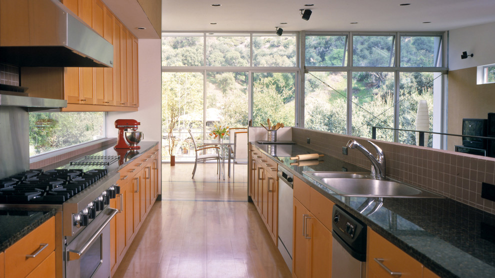 Bild på ett mellanstort 60 tals kök, med en dubbel diskho, luckor med infälld panel, skåp i mellenmörkt trä, granitbänkskiva, rött stänkskydd, stänkskydd i porslinskakel, rostfria vitvaror och ljust trägolv