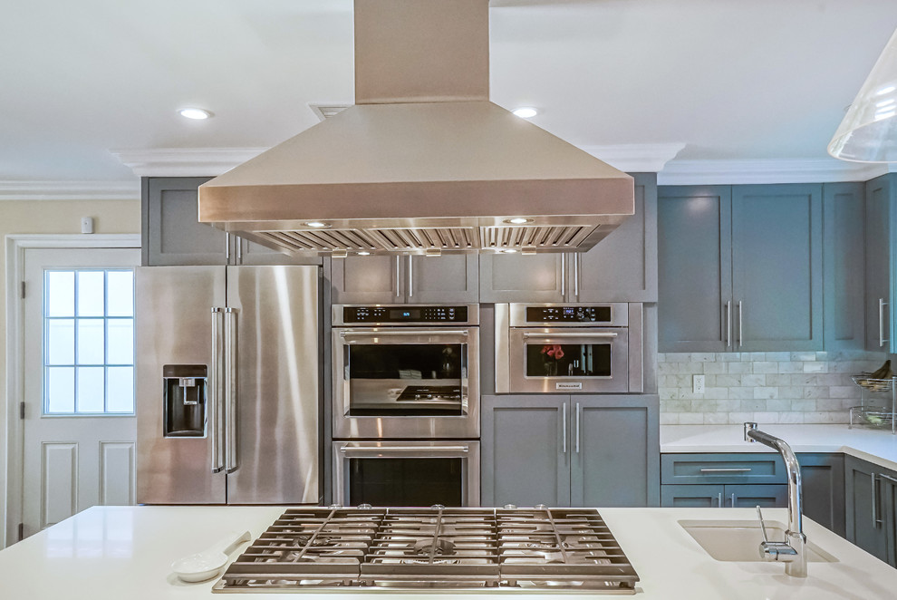 Large classic l-shaped open plan kitchen in Los Angeles with a belfast sink, shaker cabinets, grey cabinets, engineered stone countertops, grey splashback, marble splashback, stainless steel appliances, porcelain flooring, an island and white floors.