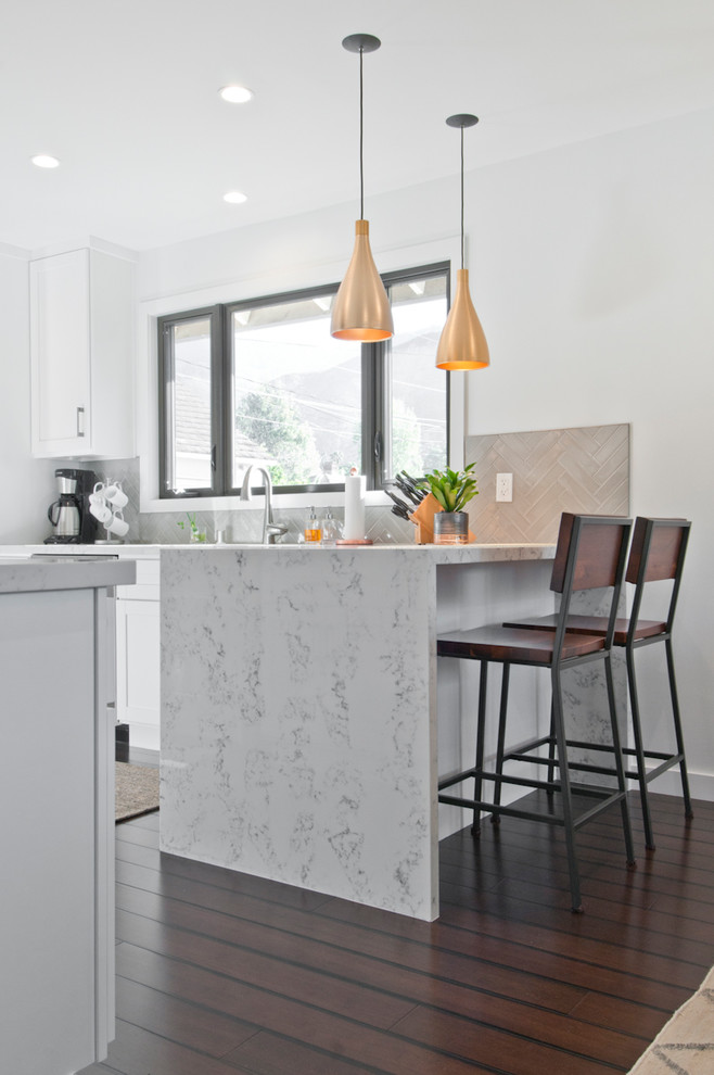 Foto på ett mellanstort kök, med en undermonterad diskho, skåp i shakerstil, vita skåp, marmorbänkskiva, grått stänkskydd, rostfria vitvaror, mörkt trägolv, en halv köksö och brunt golv