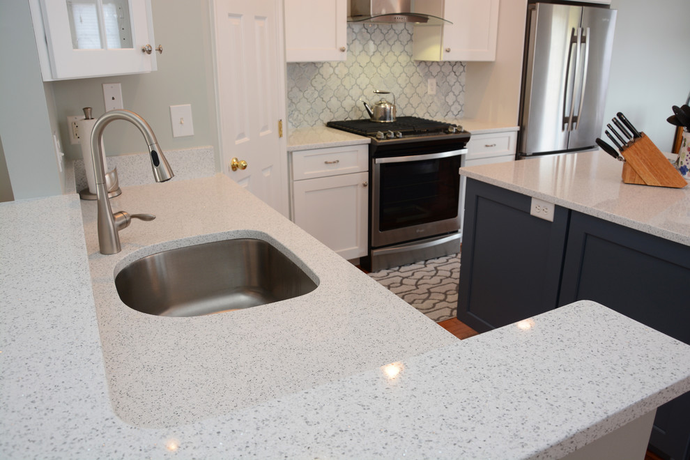 Mid-sized transitional l-shaped medium tone wood floor and brown floor eat-in kitchen photo in Baltimore with a single-bowl sink, recessed-panel cabinets, white cabinets, quartz countertops, white backsplash, stainless steel appliances and an island