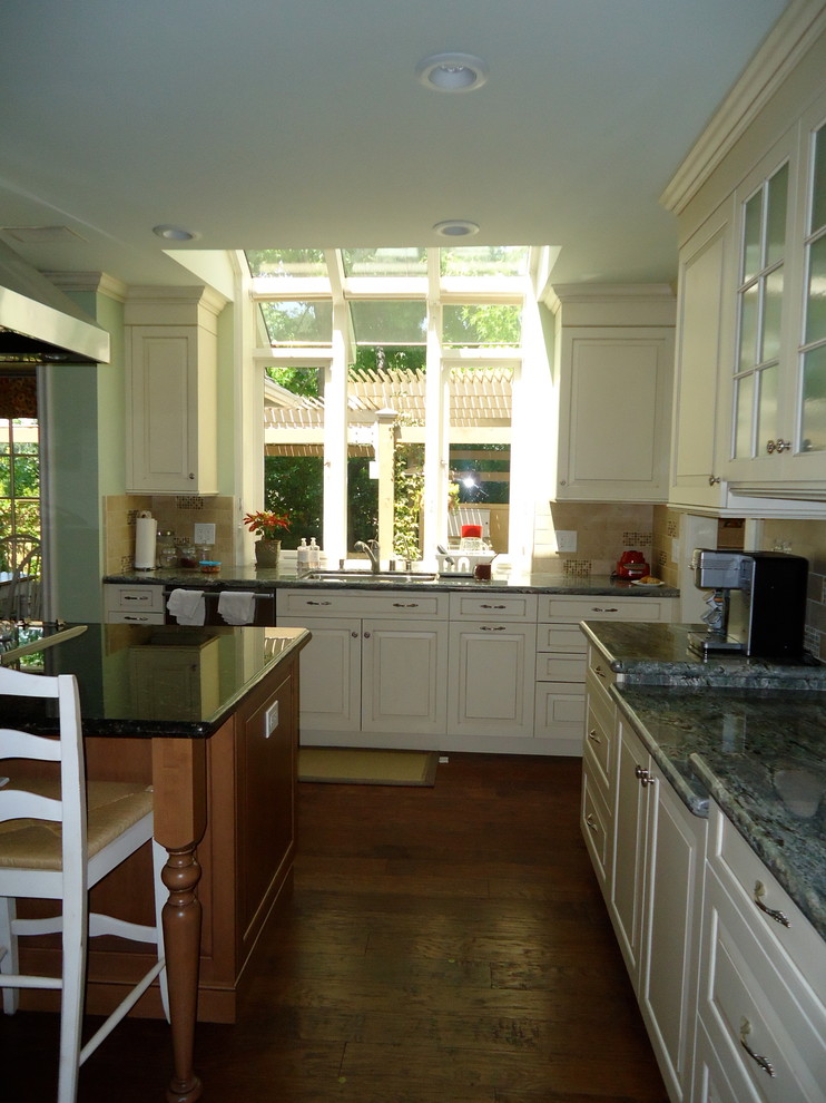 Example of a large classic medium tone wood floor enclosed kitchen design in Los Angeles with an undermount sink, raised-panel cabinets, white cabinets, granite countertops, beige backsplash, stone tile backsplash, stainless steel appliances and an island