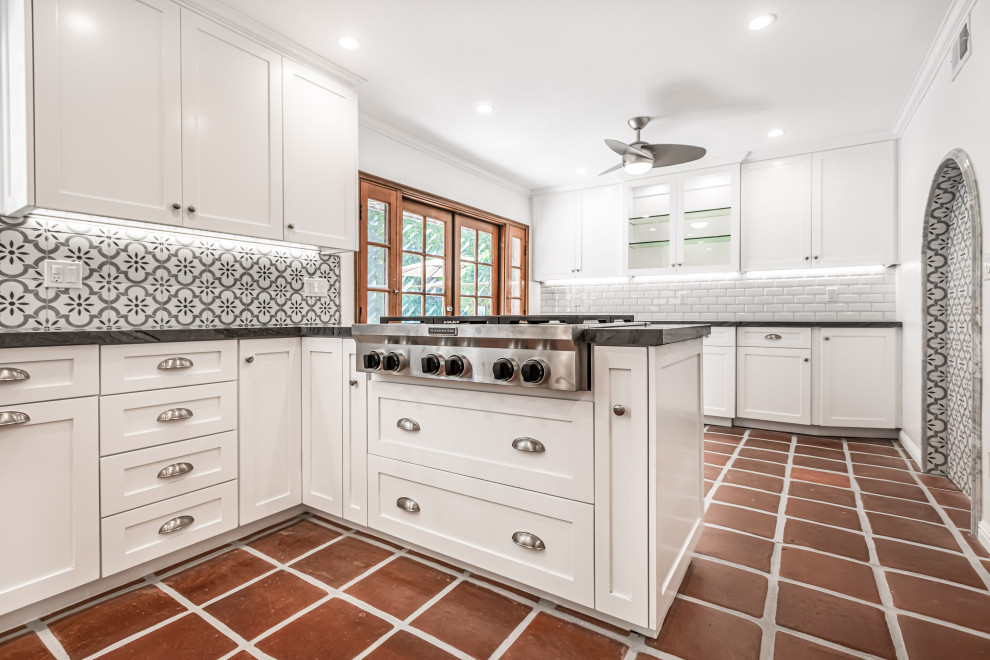 Foto på ett mellanstort lantligt grå kök, med en rustik diskho, skåp i shakerstil, vita skåp, bänkskiva i kvartsit, grått stänkskydd, stänkskydd i keramik, rostfria vitvaror, klinkergolv i terrakotta, en halv köksö och rött golv