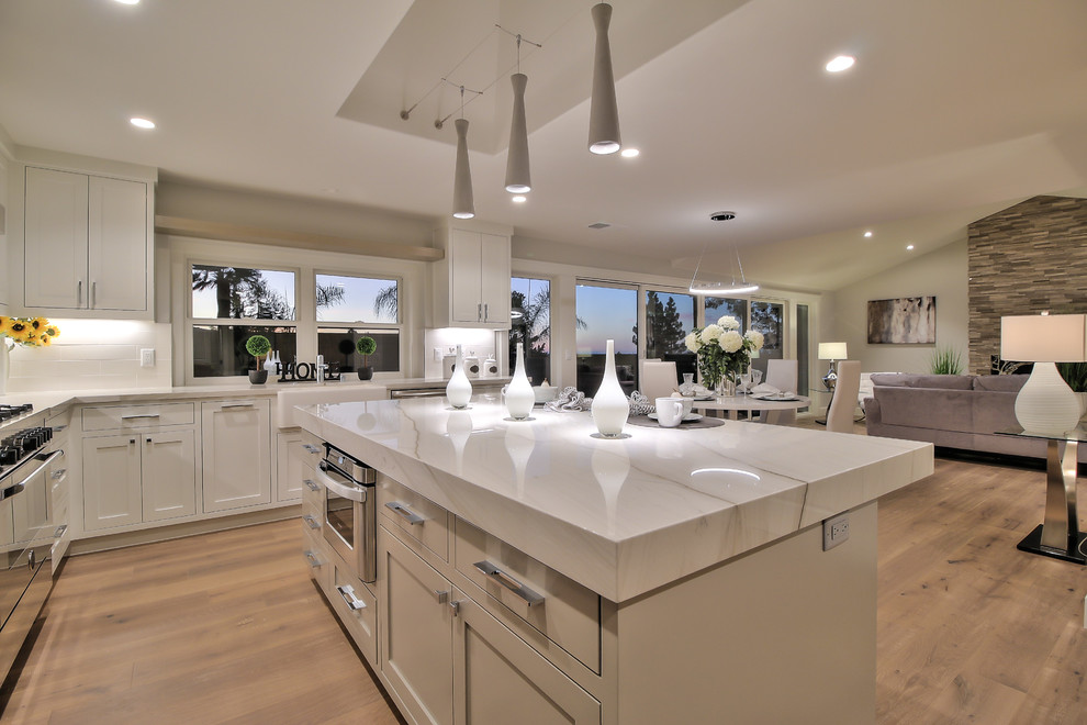 Inspiration for a modern l-shaped light wood floor and green floor eat-in kitchen remodel in San Francisco with a farmhouse sink, shaker cabinets, white cabinets, quartzite countertops, white backsplash, porcelain backsplash, stainless steel appliances and an island