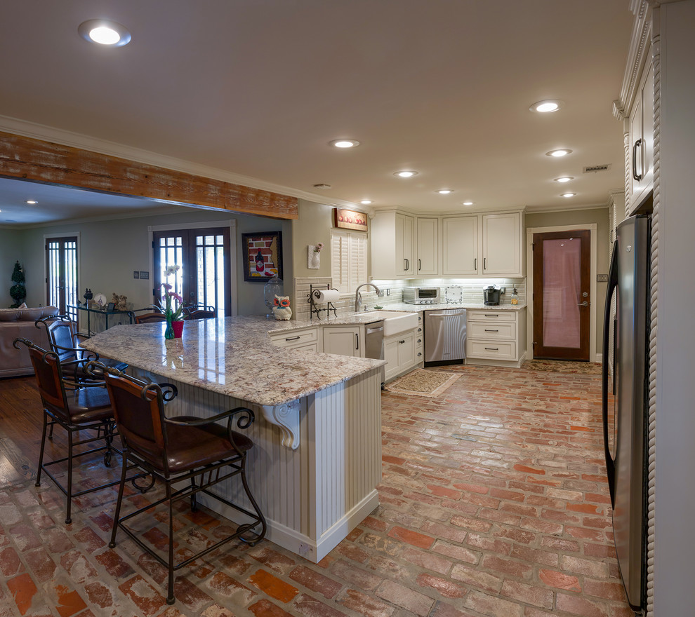 Mid-sized transitional l-shaped brick floor eat-in kitchen photo in New Orleans with a peninsula, a farmhouse sink, beaded inset cabinets, white cabinets, granite countertops, green backsplash, subway tile backsplash and stainless steel appliances