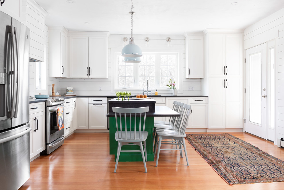 Inspiration for a large farmhouse l-shaped kitchen/diner in Boston with a submerged sink, shaker cabinets, white cabinets, engineered stone countertops, white splashback, wood splashback, stainless steel appliances, medium hardwood flooring, an island, black worktops and brown floors.