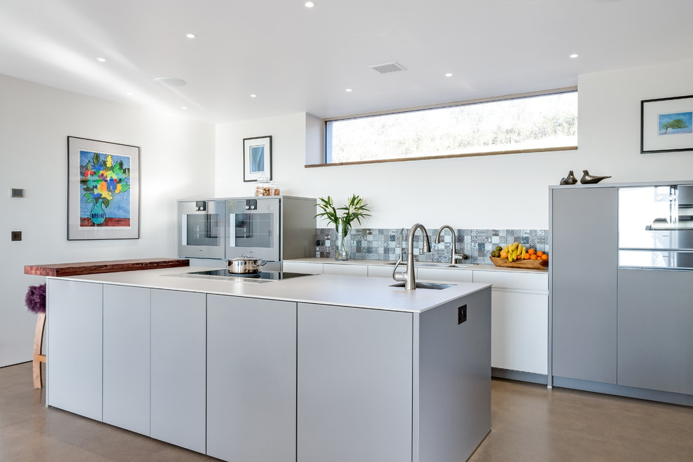 Large contemporary kitchen in Gloucestershire with grey cabinets, composite countertops, grey splashback, concrete flooring, an island, a submerged sink, flat-panel cabinets and brown floors.
