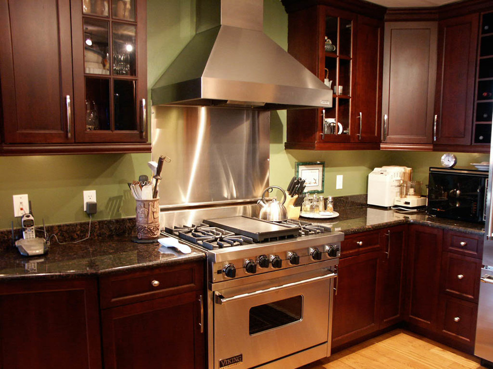 Immagine di una cucina design di medie dimensioni con ante a filo, ante in legno bruno, top in granito, elettrodomestici in acciaio inossidabile e parquet chiaro